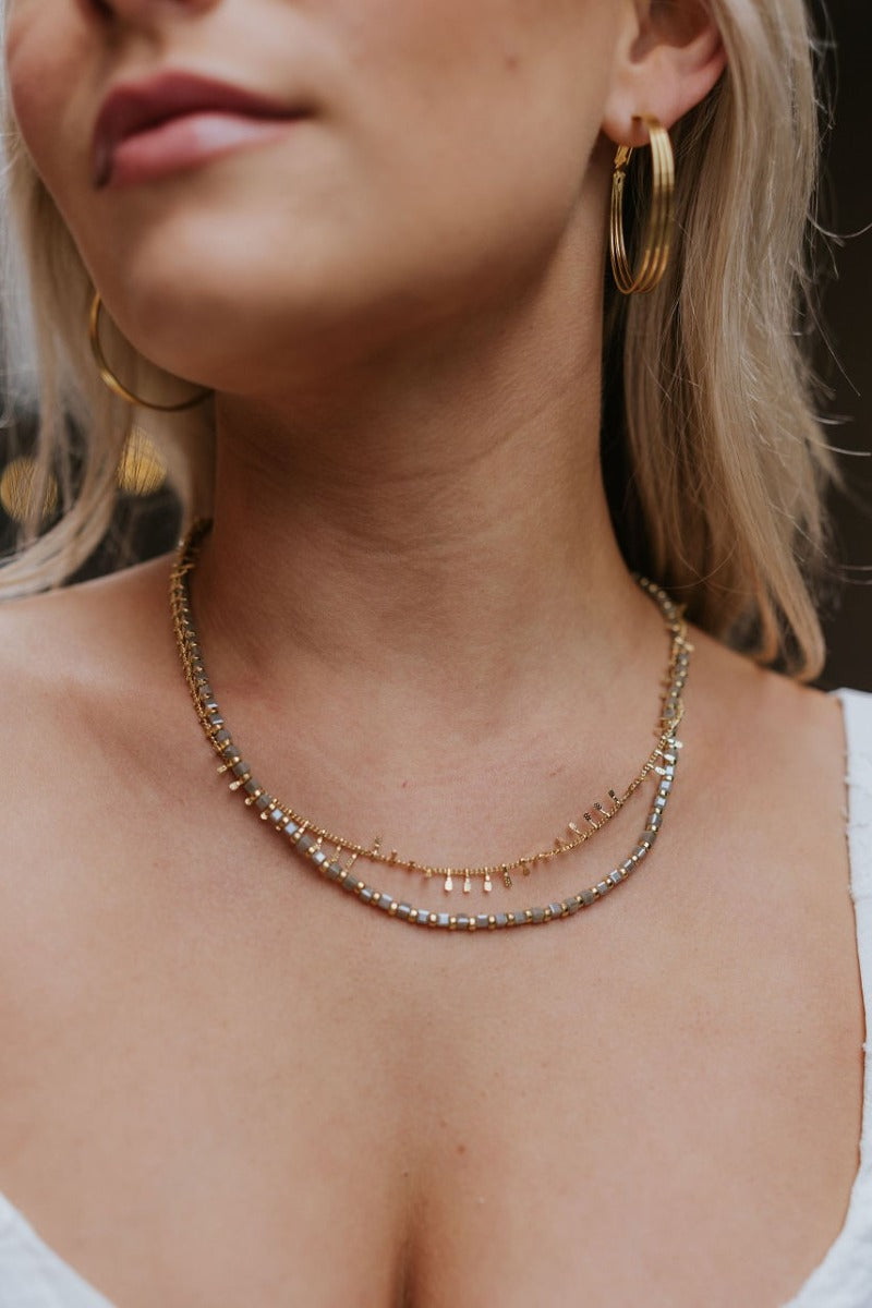 Front image of model wearing the Should've Known Necklace that has a double gold chain with iridescent grey and gold beads.