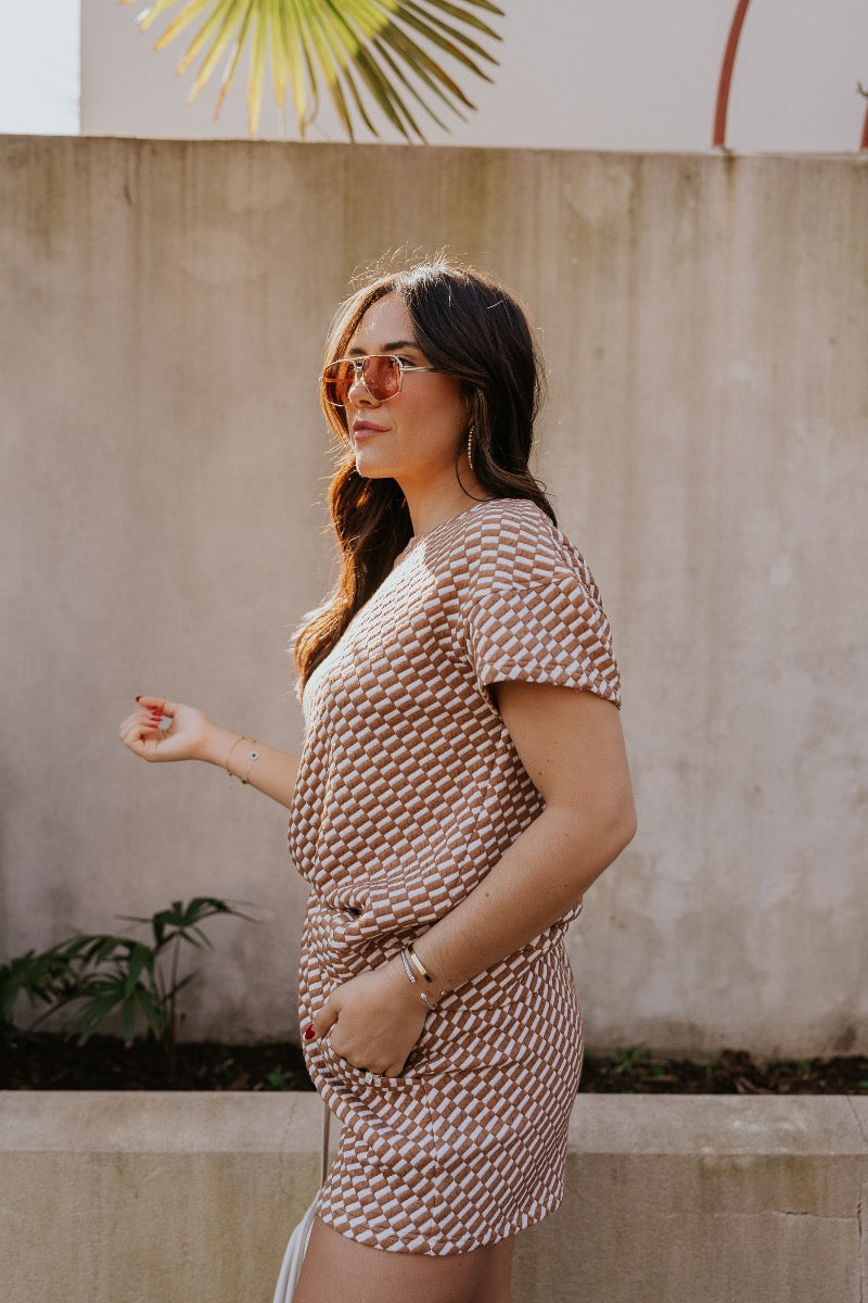 side view of model wearing The Corsica Knit Checkered Top features light brown and off white textured knit fabric, skinny checkered pattern, thick hem, round neckline and short sleeves.