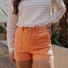 front view of model wearing The Monaco Orange Denim Shorts features washed orange denim fabric, two front pockets, two back pockets, front zipper with button closure and belt loops.