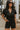 Front view of model wearing the Dakota Denim Romper in Black that has black denim fabric, front pockets, a hidden front zipper, a collared neckline, a monochromatic belt at the waistline, and short sleeves