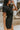 Close side view of model wearing the Dakota Denim Romper in Black that has black denim fabric, front pockets, a hidden front zipper, a collared neckline, a monochromatic belt at the waistline, and short sleeves