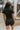Back view of model wearing the Dakota Denim Romper in Black that has black denim fabric, front pockets, a hidden front zipper, a collared neckline, a monochromatic belt at the waistline, and short sleeves