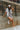 Full body view of model wearing the Head In The Clouds Romper which features light grey knit fabric, pockets on each side, a quarter button-up with wooden buttons, a round neckline, and thick straps.