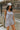 Side view of model wearing the Head In The Clouds Romper which features light grey knit fabric, pockets on each side, a quarter button-up with wooden buttons, a round neckline, and thick straps.