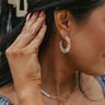 Close up view of model wearing the Rome Hoop Earring which features gold hoops with clear emerald shaped stones.