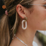 Close up view of model wearing the It Comes Natural Earrings which features green marble oval shaped hoop linked with a natural marble oval shaped hoop.