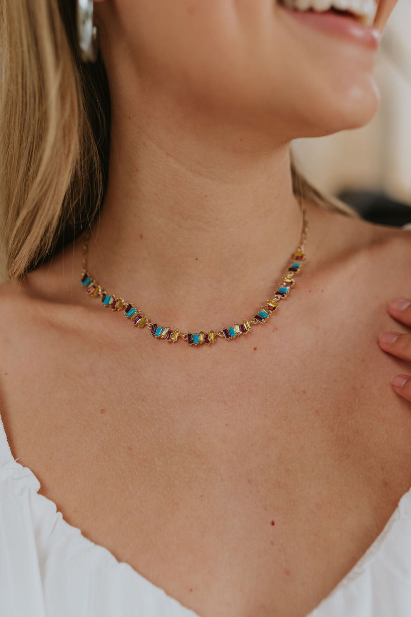 Close up view of model wearing the Something Beautiful Multi Necklace which features single gold chain link, clusters of purple, pink, yellow and turquoise stones and hook clasp closure. 