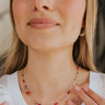 Close up view of model wearing the Float Away Necklace which features double dainty gold chain links with pink, green, purple, blue and yellow stones, and hook clasp closure.
