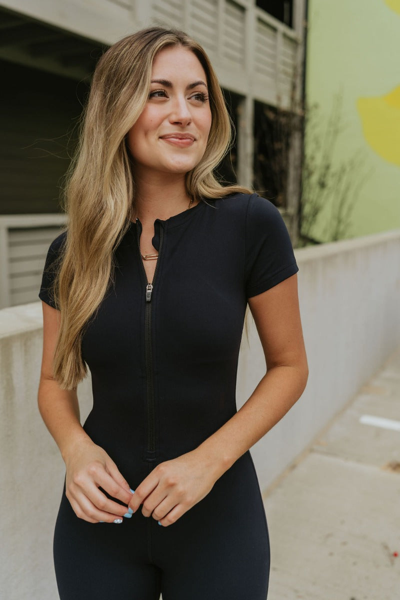 Close front view of model wearing the Bring It On Romper that has black stretchy fabric, a romper body, a monochromatic front zipper, a round neckline, and short sleeves.