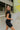 Side view of model wearing the Bring It On Romper that has black stretchy fabric, a romper body, a monochromatic front zipper, a round neckline, and short sleeves.