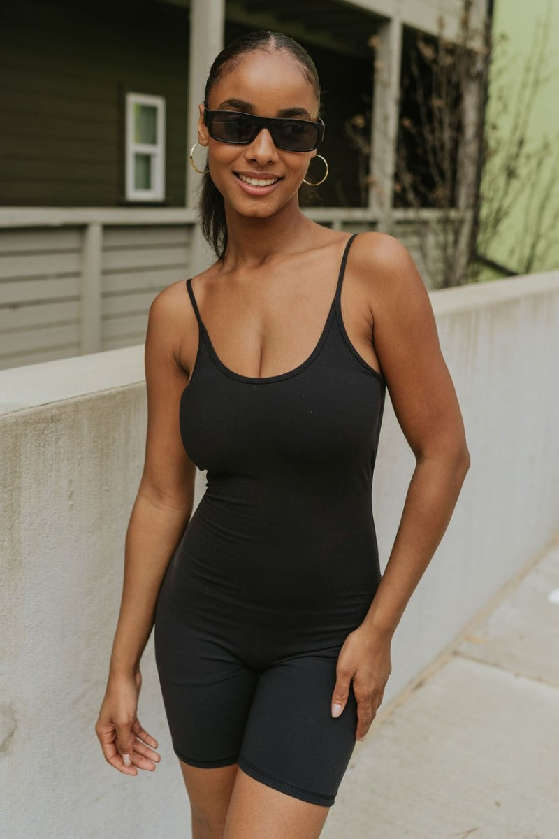 Front view of model wearing the Call It Even Romper that features black stretch fabric, a romper body, a round neckline, bra padding, and adjustable spaghetti straps.