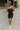 Full front view of model wearing the Call It Even Romper that features black stretch fabric, a romper body, a round neckline, bra padding, and adjustable spaghetti straps.