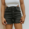 Front view of model wearing the Just USA Denim: Dream On Shorts in Washed Black which features washed black denim fabric, a high-rise waist with belt loops, a five-button fly with black buttons, two front pockets, two back pockets, distressed detailing, a