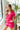 Frontal side view of model wearing the Dakota Denim Romper in Pink that has hot pink denim fabric, front pockets, a hidden front zipper, a collared neckline, a monochromatic belt at the waistline, and short sleeves
