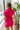 Back view of model wearing the Dakota Denim Romper in Pink that has hot pink denim fabric, front pockets, a hidden front zipper, a collared neckline, a monochromatic belt at the waistline, and short sleeves