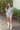 Full front view of model wearing the She's A Star Denim Romper that has light denim fabric, pockets on each side, silver buttons, silver sequin star patches, a collared neckline, short puff sleeves, and denim tie belt around the waist