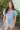Front view of model wearing the She's A Star Denim Romper that has light denim fabric, pockets on each side, silver buttons, silver sequin star patches, a collared neckline, short puff sleeves, and denim tie belt around the waist