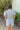 Close back view of model wearing the She's A Star Denim Romper that has light denim fabric, pockets on each side, silver buttons, silver sequin star patches, a collared neckline, short puff sleeves, and denim tie belt around the waist