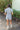 Full back view of model wearing the She's A Star Denim Romper that has light denim fabric, pockets on each side, silver buttons, silver sequin star patches, a collared neckline, short puff sleeves, and denim tie belt around the waist