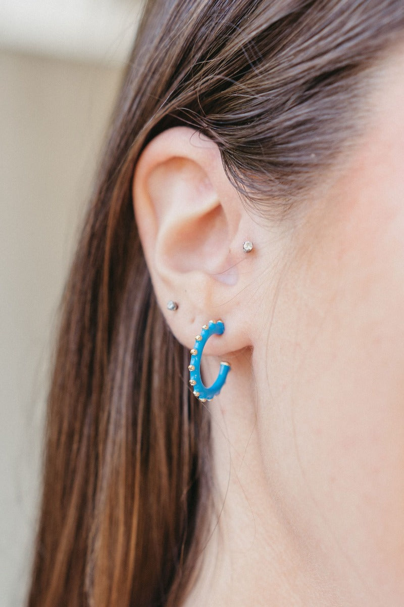 Model is wearing the Paint The Town Earring in Blue that have blue mini open shaped hoop with gold dots.