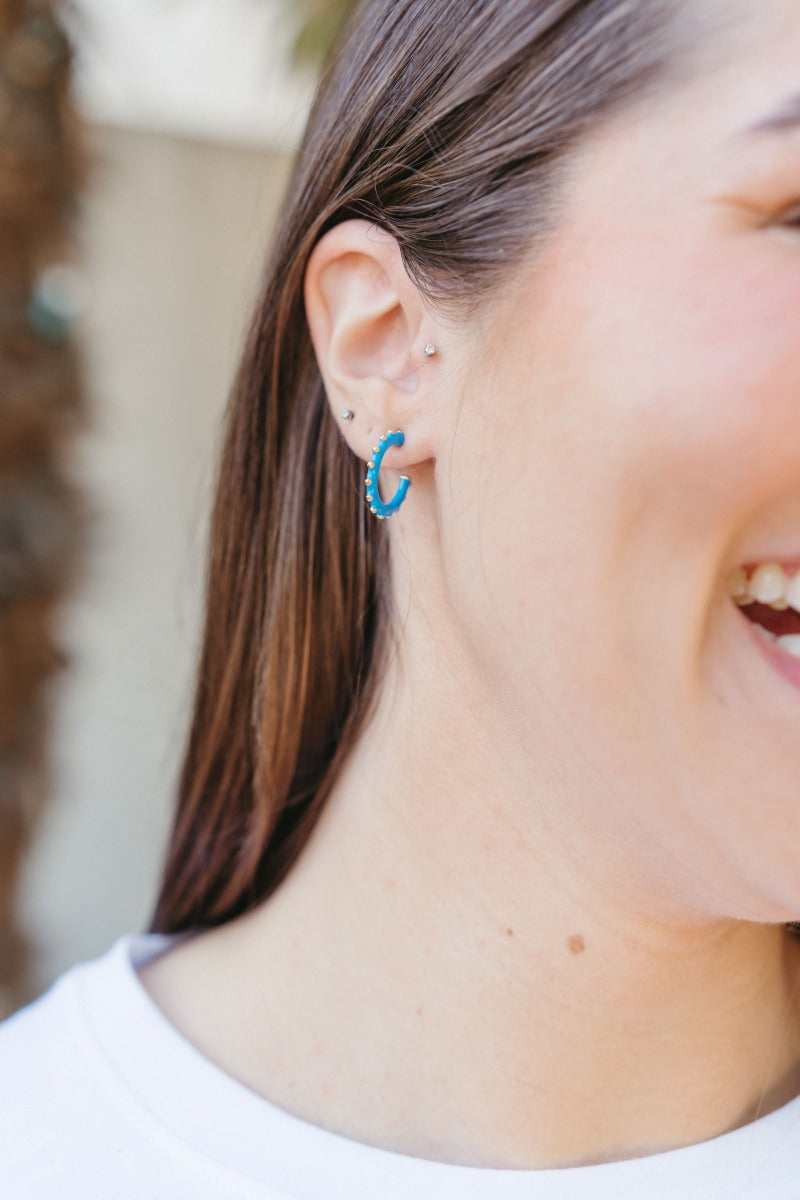 Model is wearing the Paint The Town Earring in Blue that have blue mini open shaped hoop with gold dots.