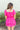 Back view of model wearing the Wishful Thinking Romper which features fuchsia fabric, a ruffle-tiered skirt, fuchsia shorts lining, an elastic waistband, a sweetheart neckline and short puff sleeves.