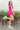 Full body side view of model wearing the Wishful Thinking Romper which features fuchsia fabric, a ruffle-tiered skirt, fuchsia shorts lining, an elastic waistband, a sweetheart neckline and short puff sleeves.
