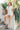Full body view of model wearing the Dakota Denim Romper in Off White which features white denim fabric, front pockets, a hidden front zipper, a collared neckline, a monochromatic belt at the waistline, and short sleeves.