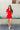 Full body view of model wearing the Dakota Denim Romper in Red which features red denim fabric, front pockets, a hidden front zipper, a collared neckline, a monochromatic belt at the waistline, and short sleeves.