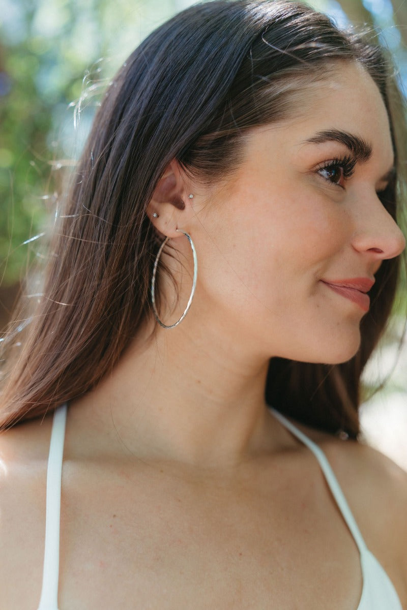 Close up side view of model wearing the On Your Own Hoop Earrings in Silver which features large closed hoop with silver hammered design.