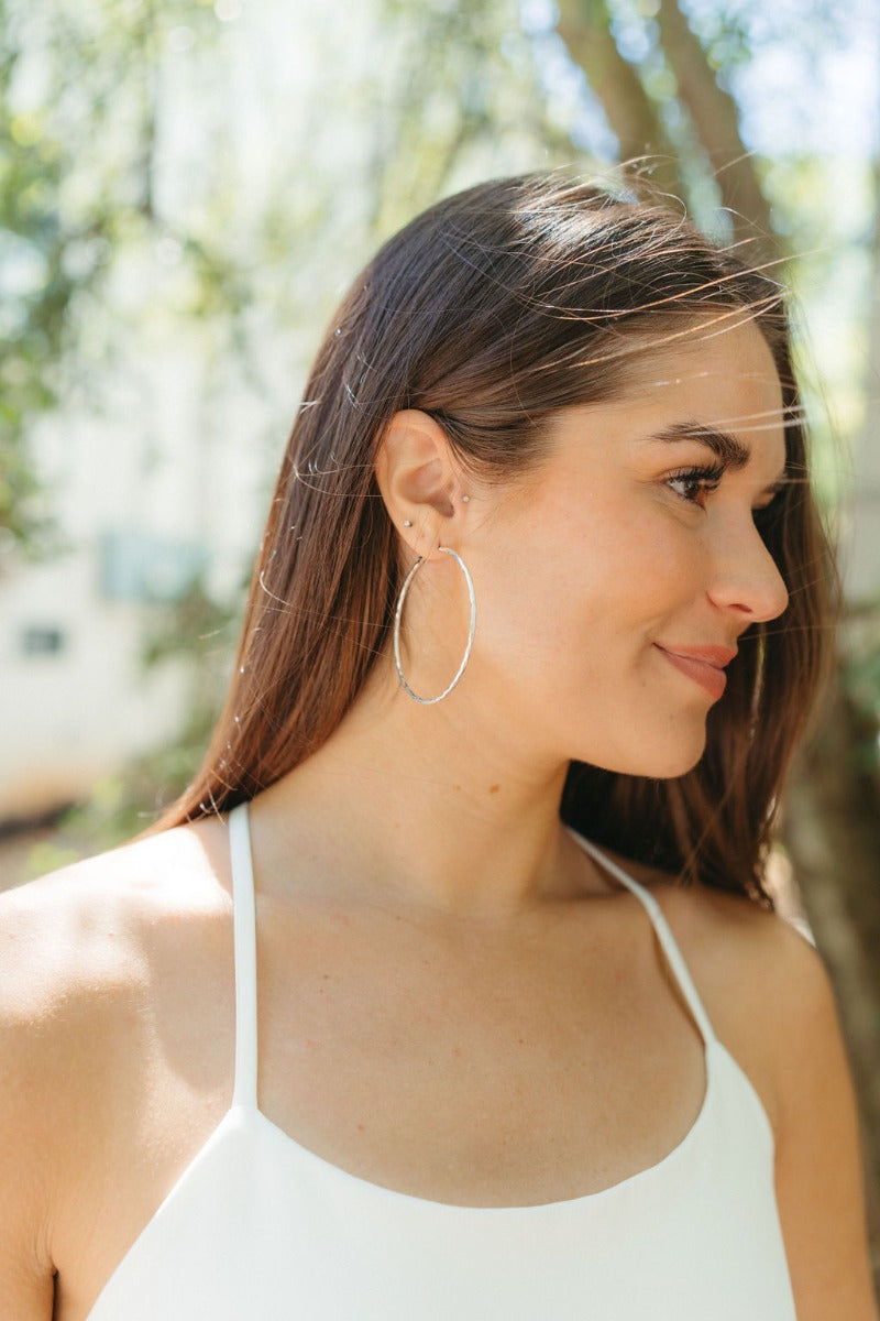 Side view of model wearing the On Your Own Hoop Earrings in Silver which features large closed hoop with silver hammered design.