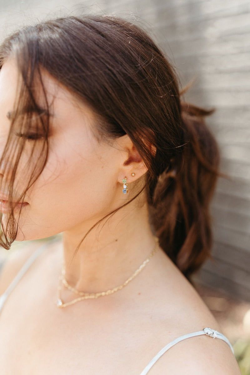 Side view of model wearing the Speak Easy Multi Hoop which features mini gold closed hoops with pearl, amber, blue and green beads.