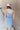 Back view of model wearing the Long Beach Dress that has light blue ribbed fabric, midi length, a round neckline, and thick straps.
