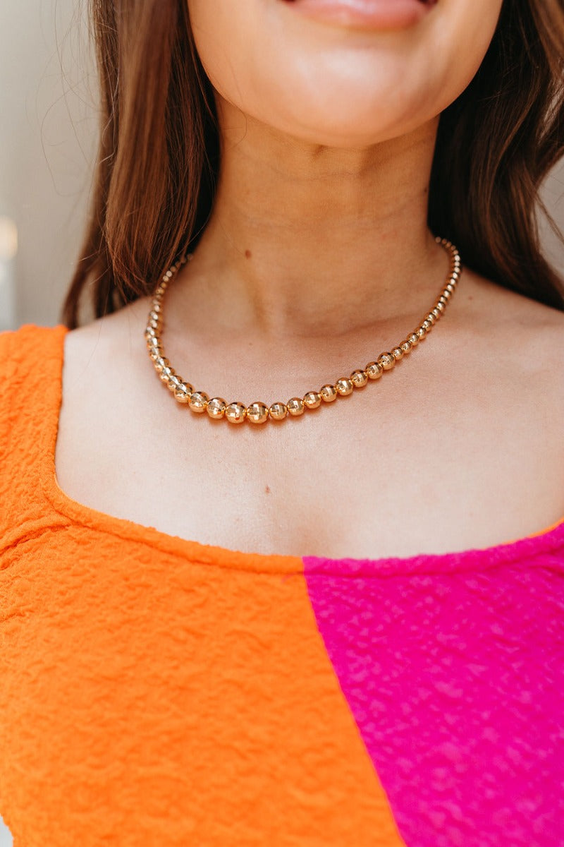 Close up view of model wearing the Let's Dance Tonight Necklace which features a shiny gold disco ball beads, hook closure and shiny gold disco ball hook earrings.
