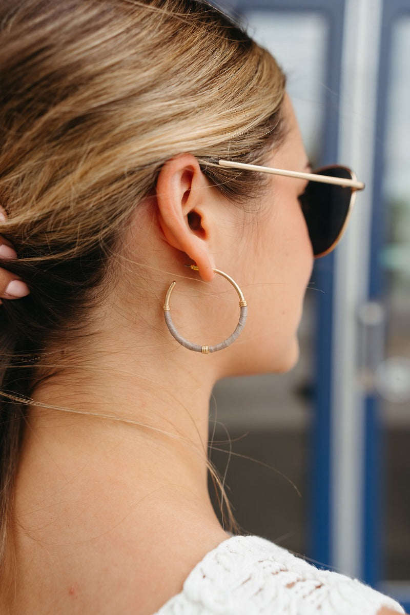 Side view of model wearing the Wrapped in You Earrings which features medium, open gold hoops wrapped with grey paper and gold details.