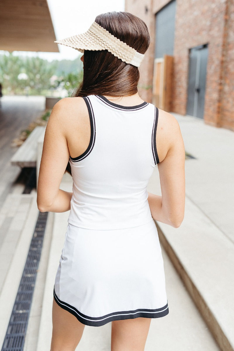 Back view of model wearing the Set For Life Tank which features white fabric, black trim, a built-in-bra, a round neckline, and a sleeveless racerback design.