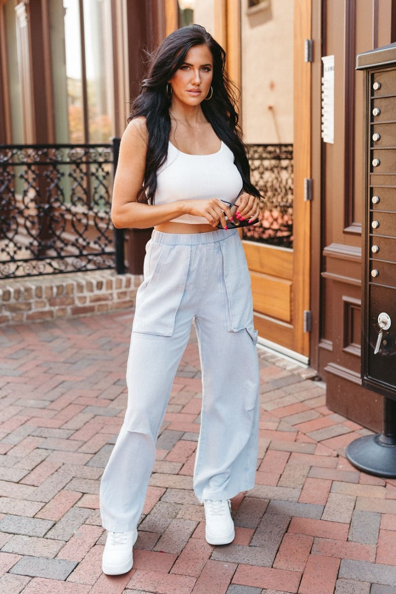 Full body front view of model wearing the Live Fast Cargo Pants that have light blue denim like fabric, two front pockets, an elastic waistband, and wide legs.