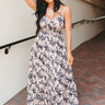 Full body view of model wearing the South Beach Floral Dress which features black fabric with a light pink, peach, lavender and tan floral pattern, a three-tiered skirt, a smocked upper, a sweetheart neckline, and adjustable straps.