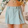 front view of model wearing the Santa Monica Pleated Skirt that has sage fabric, pleated details, a front zipper with a hook closure, belt loops, and back pockets