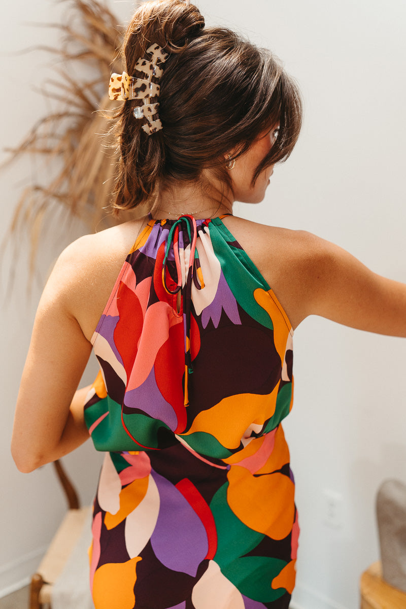 Back view of model wearing the When In Rome Multi Tank which features plum, orange, lavender, red, green, pink and cream lightweight fabric, floral print, high neckline, sleeveless and back key hole with adjustable strap ties.