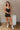 Full body view of model wearing the Spin Me Around Romper which features washed black denim, two front pockets, a sweetheart neckline, adjustable straps, an open back with corset ties, and a back zipper.