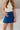 Front view of model wearing the Roll With It Skirt which features royal blue fabric, pleated details, royal blue shorts lining and a monochromatic side zipper with a hook closure.