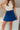 Front view of model wearing the Roll With It Skirt which features royal blue fabric, pleated details, royal blue shorts lining and a monochromatic side zipper with a hook closure.