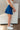 Side view of model wearing the Roll With It Skirt which features royal blue fabric, pleated details, royal blue shorts lining and a monochromatic side zipper with a hook closure.