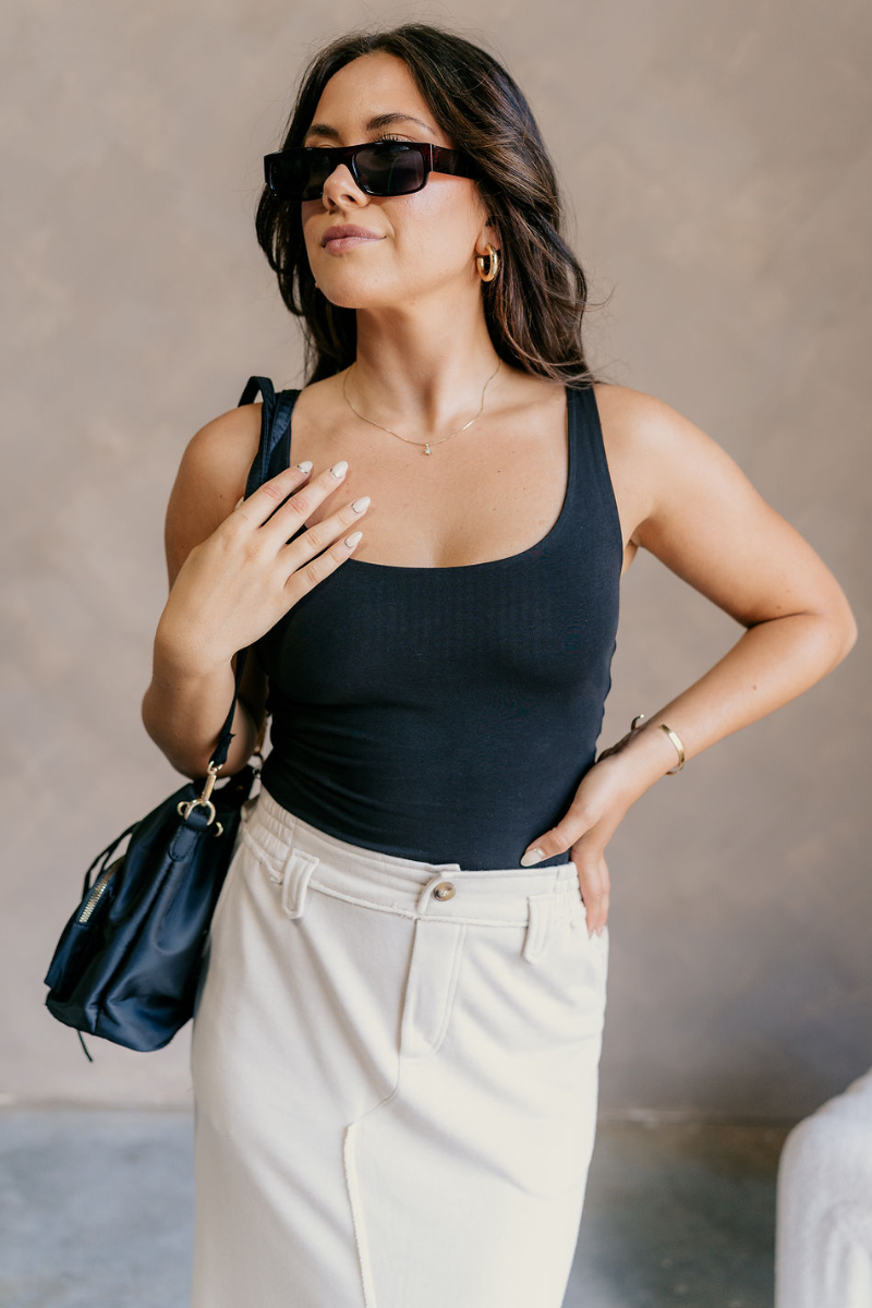 Close up view of model wearing the Josie Black Basic Scoop Neck Tank which features stretchy double-layered black knit fabric, an elastic hem, a scooped neckline, and thick straps.
