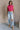 Full body view of model wearing the Kelly Pink Cropped Turtleneck Sweater which features hot pink cable knit fabric, a cropped waist, a turtleneck neckline, and a sleeveless design.