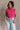 Front view of model wearing the Kelly Pink Cropped Turtleneck Sweater which features hot pink cable knit fabric, a cropped waist, a turtleneck neckline, and a sleeveless design.