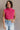 Front view of model wearing the Kelly Pink Cropped Turtleneck Sweater which features hot pink cable knit fabric, a cropped waist, a turtleneck neckline, and a sleeveless design.
