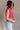 Side view of model wearing the Kelly Pink Cropped Turtleneck Sweater which features hot pink cable knit fabric, a cropped waist, a turtleneck neckline, and a sleeveless design.