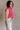 Side view of model wearing the Kelly Pink Cropped Turtleneck Sweater which features hot pink cable knit fabric, a cropped waist, a turtleneck neckline, and a sleeveless design.